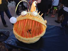 a group of people standing around a carved pumpkin with googly eyes and carrots on it