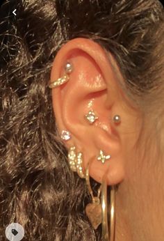 a close up of a person with ear piercings on their ears and in the background are curly hair