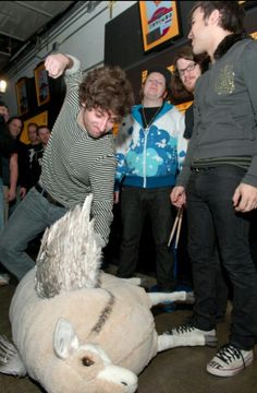 a group of young men standing around a stuffed animal on the floor in front of them