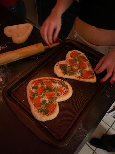 two heart shaped pizzas are being prepared on a baking sheet for the oven to bake