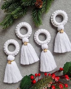 four white tasseled earrings on top of a table next to holly branches and pine cones