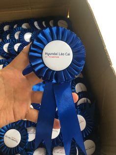 a person is holding a blue ribbon in front of many other ribbons on the box