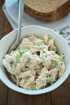 a white bowl filled with chicken salad next to two slices of bread