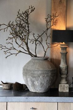 a vase sitting on top of a table next to a lamp and some branches in it