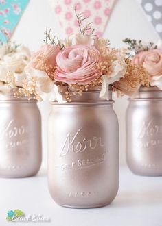 three mason jars with flowers in them are sitting on a table next to a bunting banner