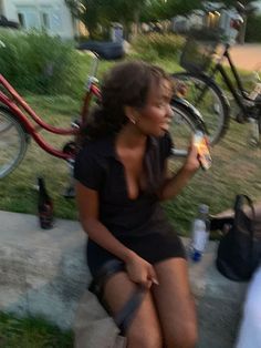 a woman is sitting on the curb eating and drinking from a bottle in her hand