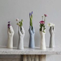 five hand - shaped vases with flowers in them