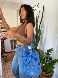 a woman holding onto a blue handbag in her right hand while standing next to a potted plant