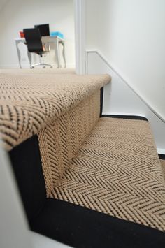 a carpeted stair case with black and tan rugs on the bottom, next to a white chair