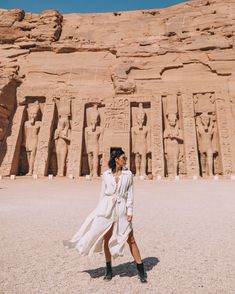 a woman standing in front of an egyptian temple wearing a white dress and black booties