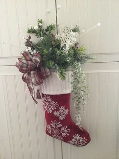 a christmas stocking hanging on the door with flowers and greenery in it,