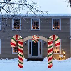 two candy canes in front of a house decorated for christmas