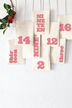 pink and gold numbers hanging from clothes pins on a white wall next to red flowers