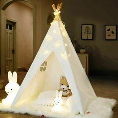 a teepee tent with lights and stuffed animals on the floor in front of it