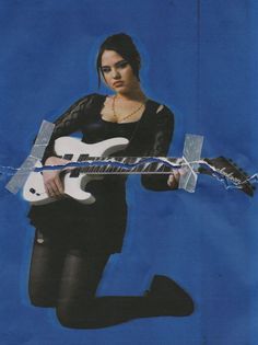 a woman holding a white electric guitar in her right hand and wearing black tights