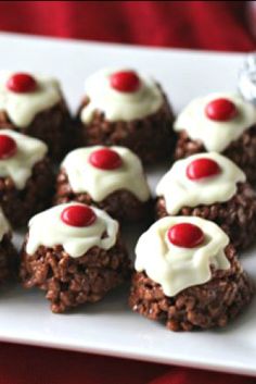 a white plate topped with cookies covered in frosting and cherries on top of a red table cloth