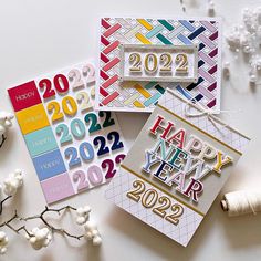 three new year's greeting cards on a table with white flowers and twine spools