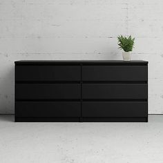 a black dresser sitting in front of a white wall with a plant on top of it