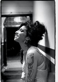 a black and white photo of a woman with tattoos on her arm, leaning against a wall