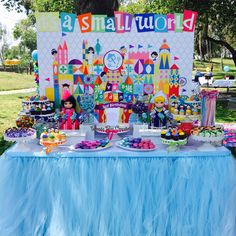 a table topped with cakes and cupcakes next to a sign that says it's a small world