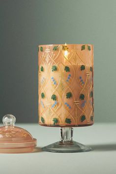 a pink candle sitting on top of a table next to a glass container with a lid