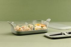 a container filled with food next to a laptop computer on a counter top in front of a green wall