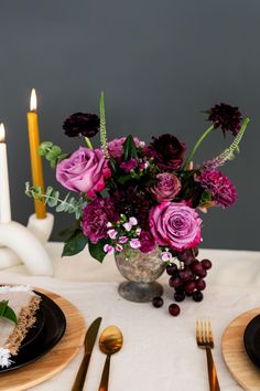 a table set for two with flowers and candles in the background, along with plates and utensils