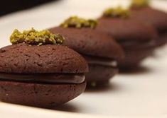 three chocolate cookies with yellow sprinkles sitting on top of each other in front of a white plate