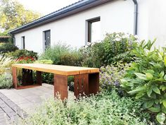 a wooden bench sitting in the middle of a garden next to a white building with windows