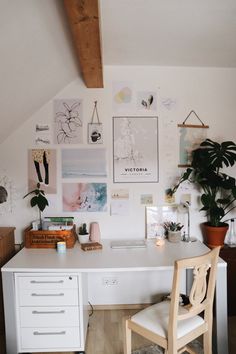 a white desk topped with a computer next to a wooden chair and potted plant