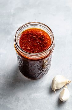 a jar filled with red sauce next to garlic