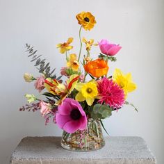 a vase filled with lots of colorful flowers on top of a cement block next to a white wall