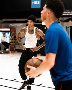 a man holding a basketball while standing next to another man in a gym with other men