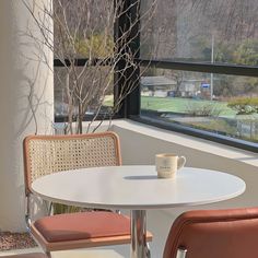 two chairs and a table with a cup on it in front of a large window