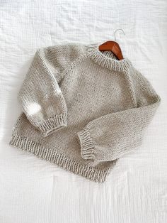 an old sweater is laying on a white bed with a wooden hanger in front of it