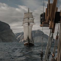 a large sailboat sailing in the ocean with mountains in the backgrouds