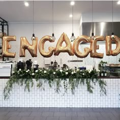 an engaged sign with flowers and greenery in front of a white tiled wall behind it