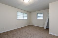 an empty room with carpet and two windows in the corner is seen from the doorway