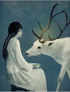 a woman sitting down next to a white deer