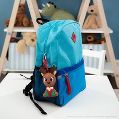 a blue backpack with a small stuffed animal on the front and back pocket, sitting on top of a white table