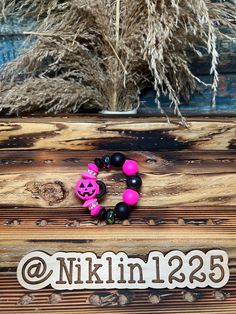 a pink and black beaded bracelet sitting on top of a wooden box next to dried grass