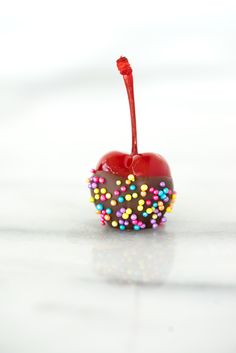 an apple with sprinkles and a red stick sticking out of it's side