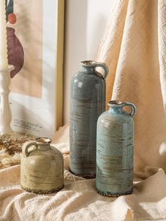 three vases sitting on top of a bed next to each other in front of a painting