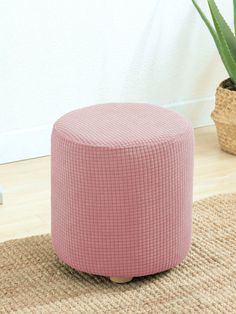 a pink ottoman sitting on top of a rug next to a potted plant