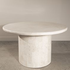 a white marble table sitting on top of a cement floor next to a gray wall