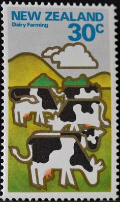 a stamp with three black and white cows standing in front of a green field under a cloudy sky