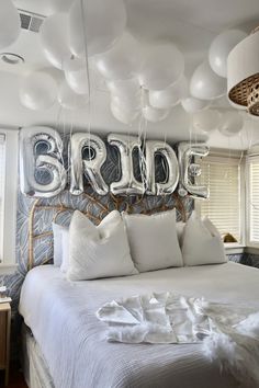 a bed with white pillows and balloons hanging from the ceiling above it that says bride