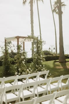 an outdoor ceremony setup with white chairs and flowers