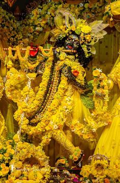 an elaborately decorated statue with flowers on it's face and arms, surrounded by yellow petals