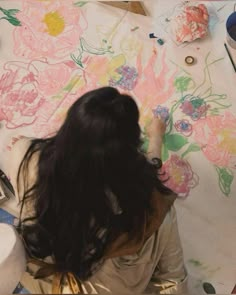 a woman sitting at a table with flowers on it and paintbrushes in front of her